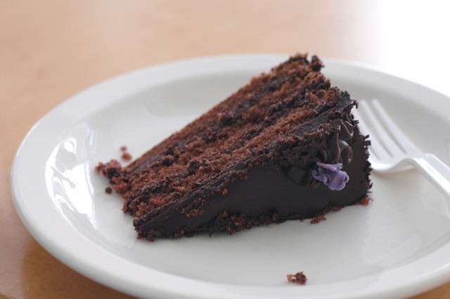 Fatia de bolo de chocolate em camadas, com cobertura brilhante, em um prato branco