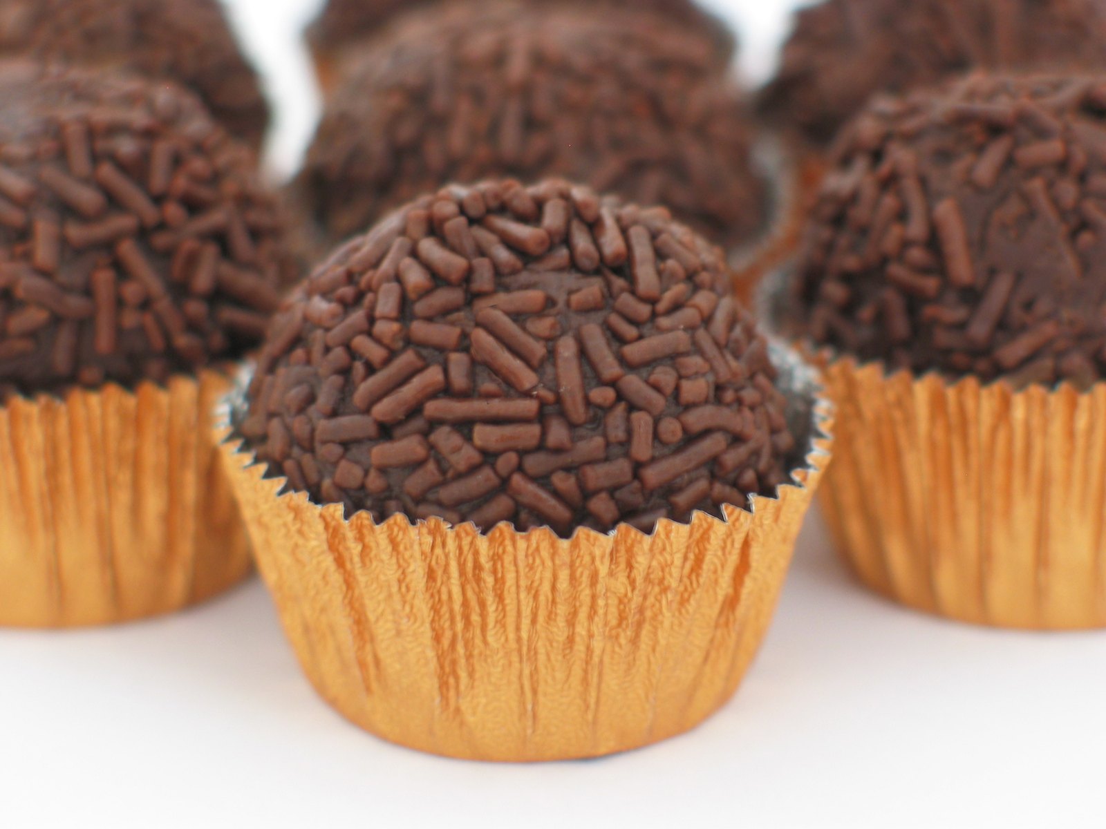 Brigadeiros enrolados no granulado de chocolate, em forminhas douradas