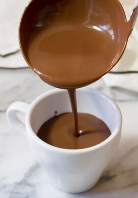 Chocolate quente sendo servido com concha em uma xícara branca