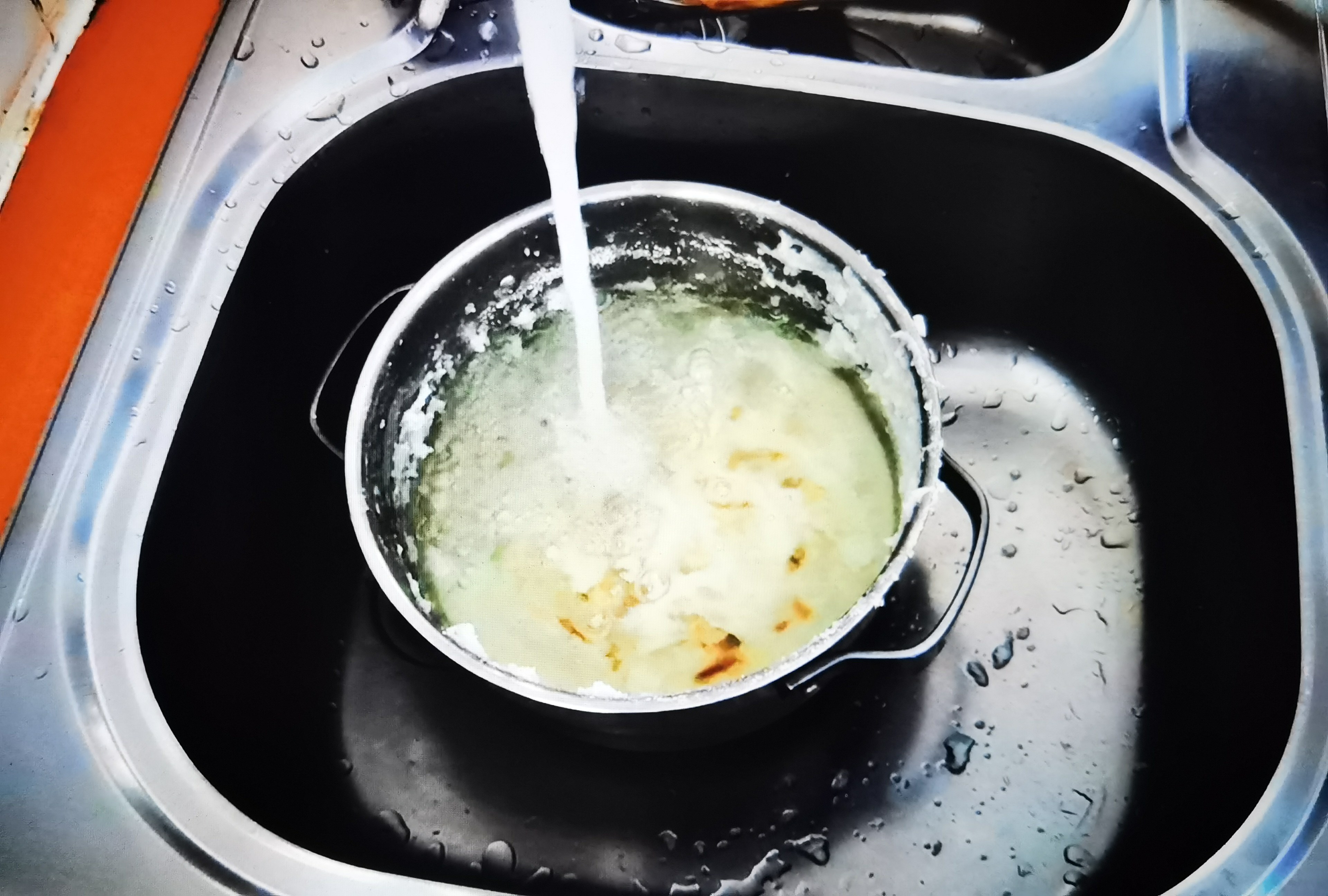 Panela na pia sendo enxaguada, o passo de amolecer o fundo