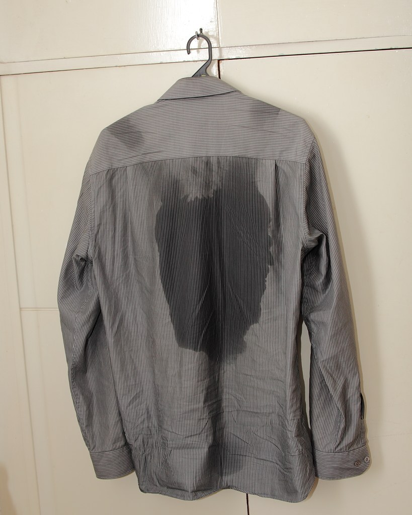 Camisa listrada no cabide com uma mancha escura de umidade nas costas
